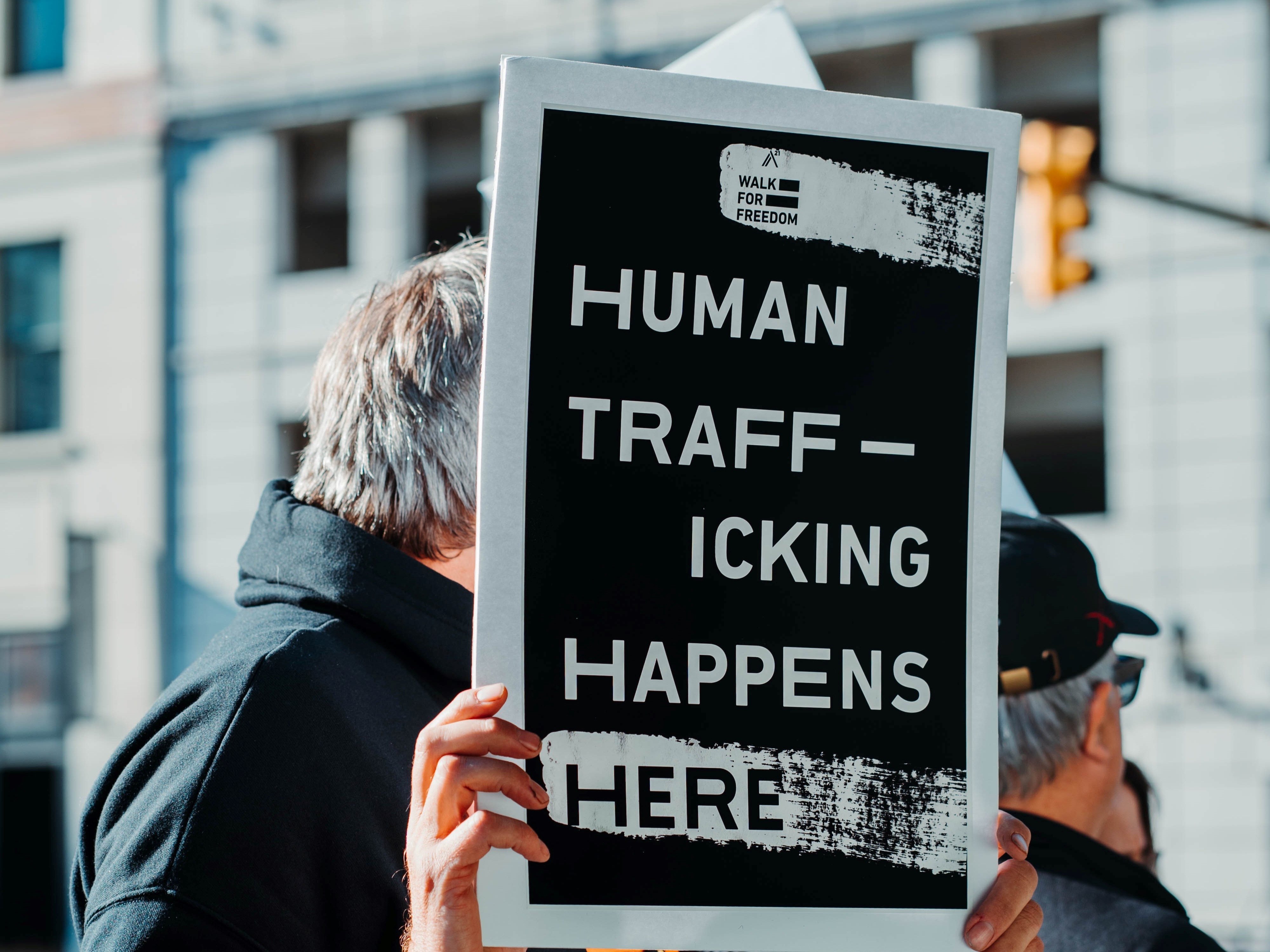Antall ofre for menneskehandel som ble oppdaget rundt om i verden falt i 2020 med 11 prosent fra året før, ifølge en ny UNODC-rapport. Her står en mann med et skilt hvor det står: «Human trafficking happens here», eller «Menneskehandel skjer her» for å sette fokus på menneskehandel som et globalt problem i dag. Foto: Hermes Rivera/Unsplash.